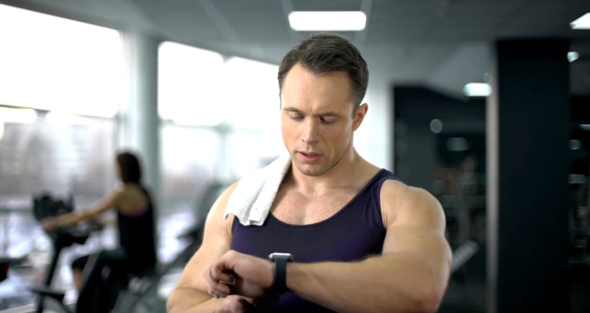 A muscular man checks his smartwatch at the gym.