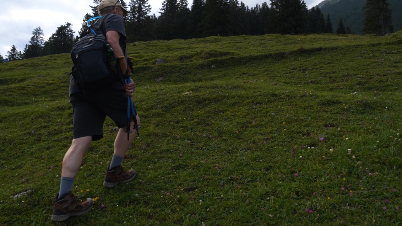 A man walks uphill on a grassy mountain trail with a backpack.