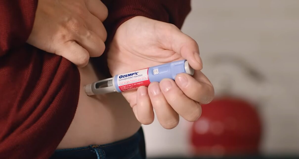 A person holds an Ozempic injection pen near the abdomen.