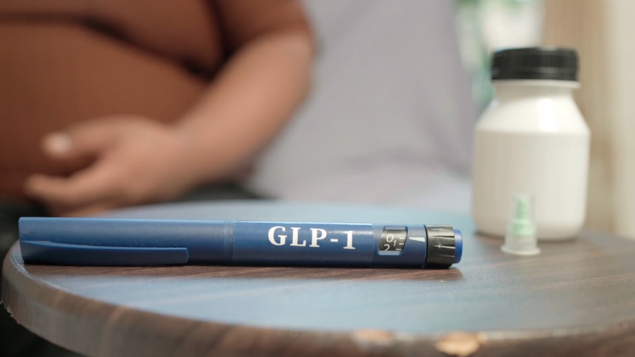 A GLP-1 injection pen sits on a table beside a medication bottle and needle cap.