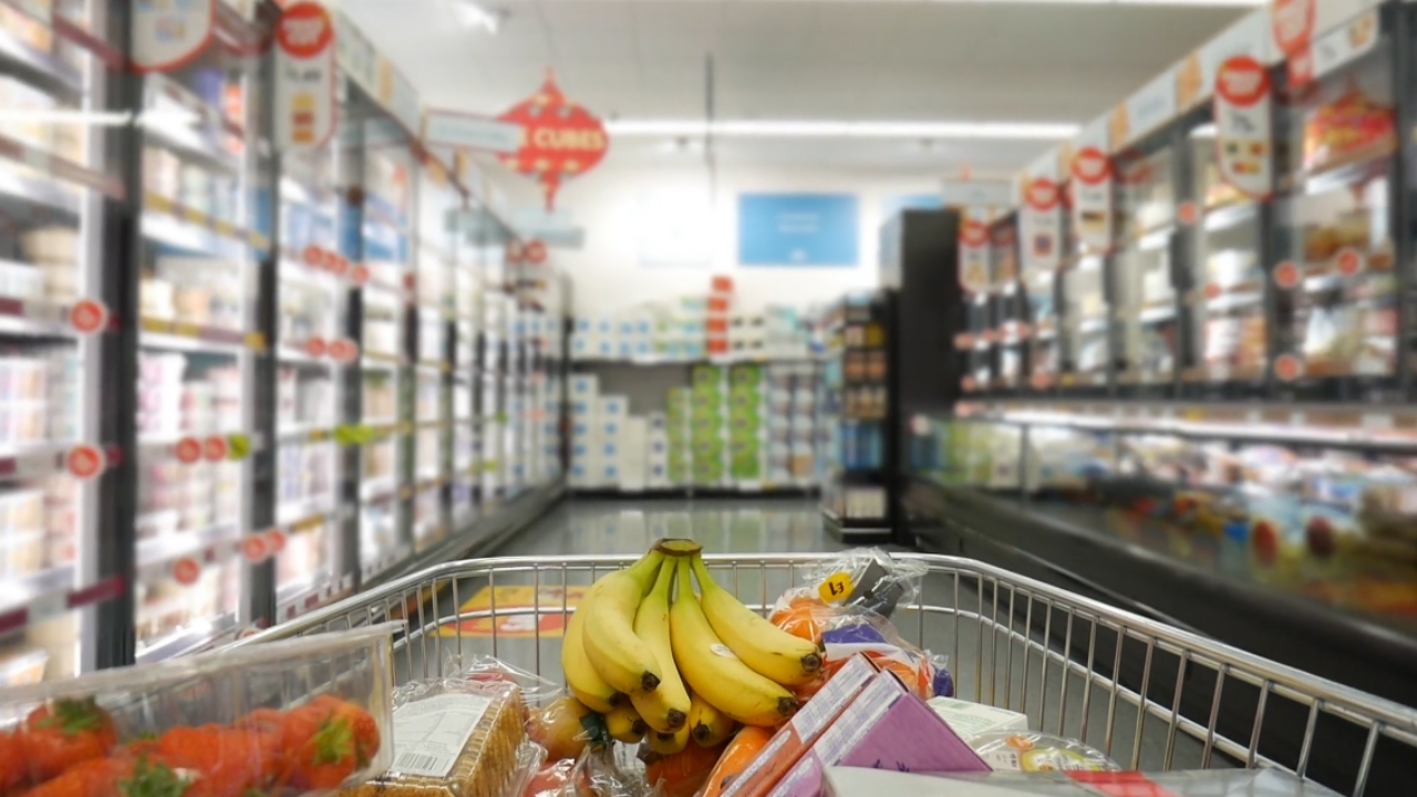 A grocery cart with bananas, strawberries, and packaged food in a supermarket aisle.
