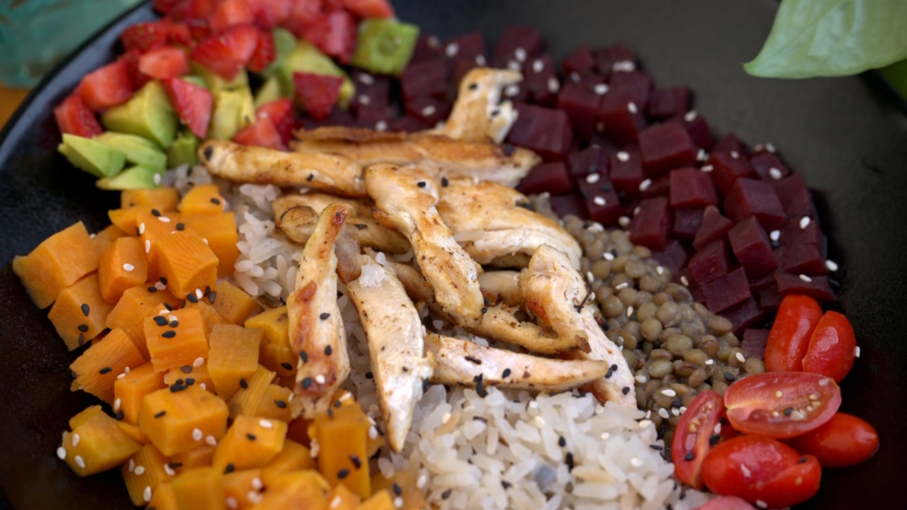 A bowl with grilled chicken, rice, sweet potato, avocado, beets, lentils, and tomatoes.