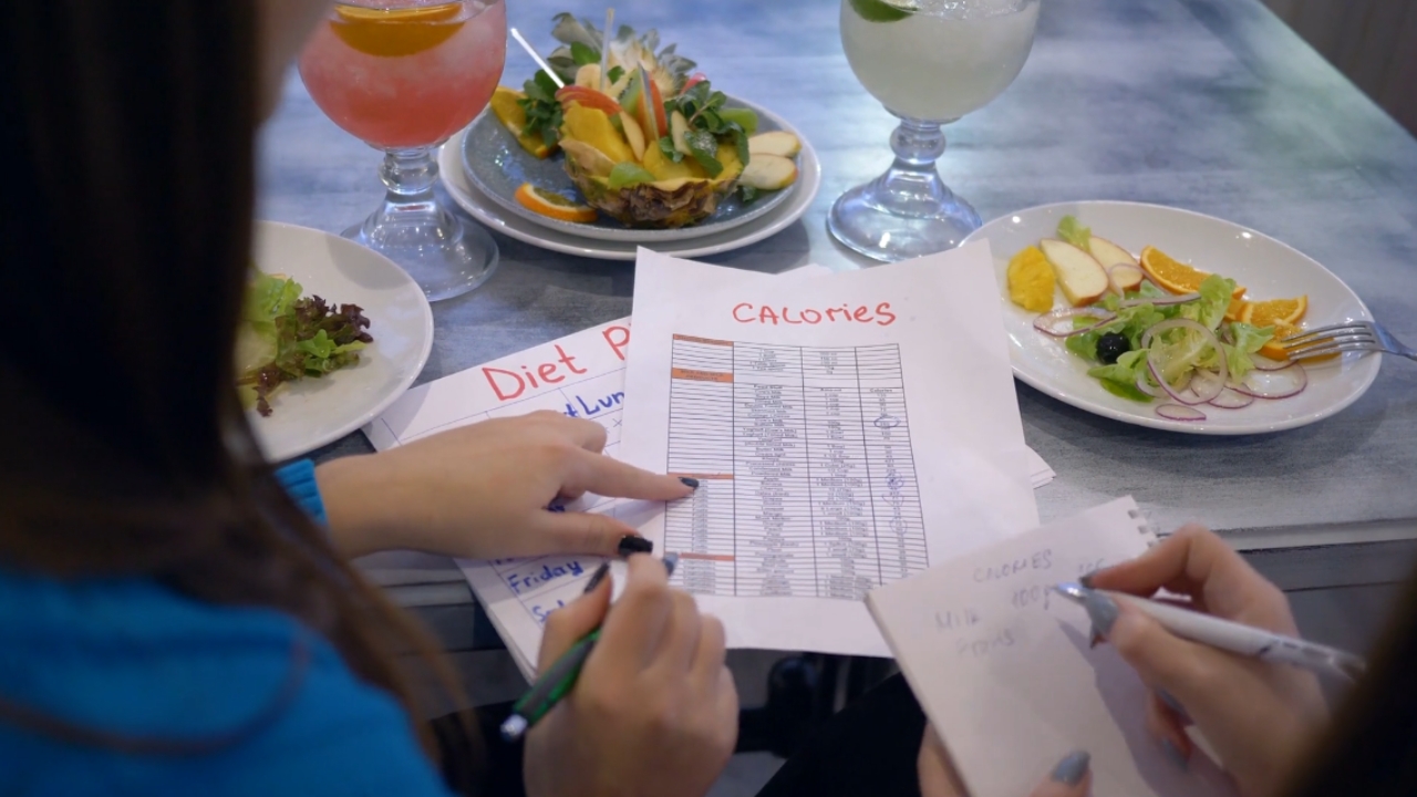 Two people review a calorie chart beside plates of food.