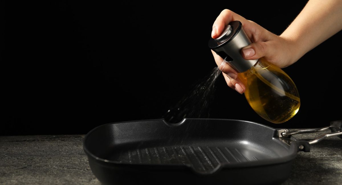 Hand spraying cooking oil into a nonstick grill pan.
