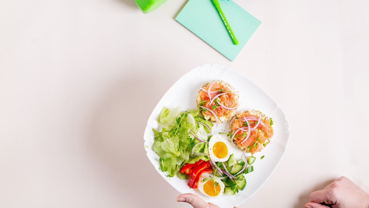 A plate of salmon toast, boiled eggs, and fresh vegetables on a white table.