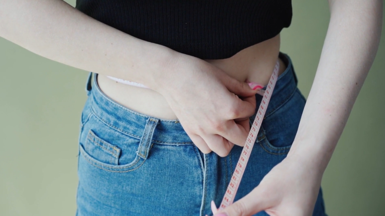 Woman measures her waist with a tape measure.