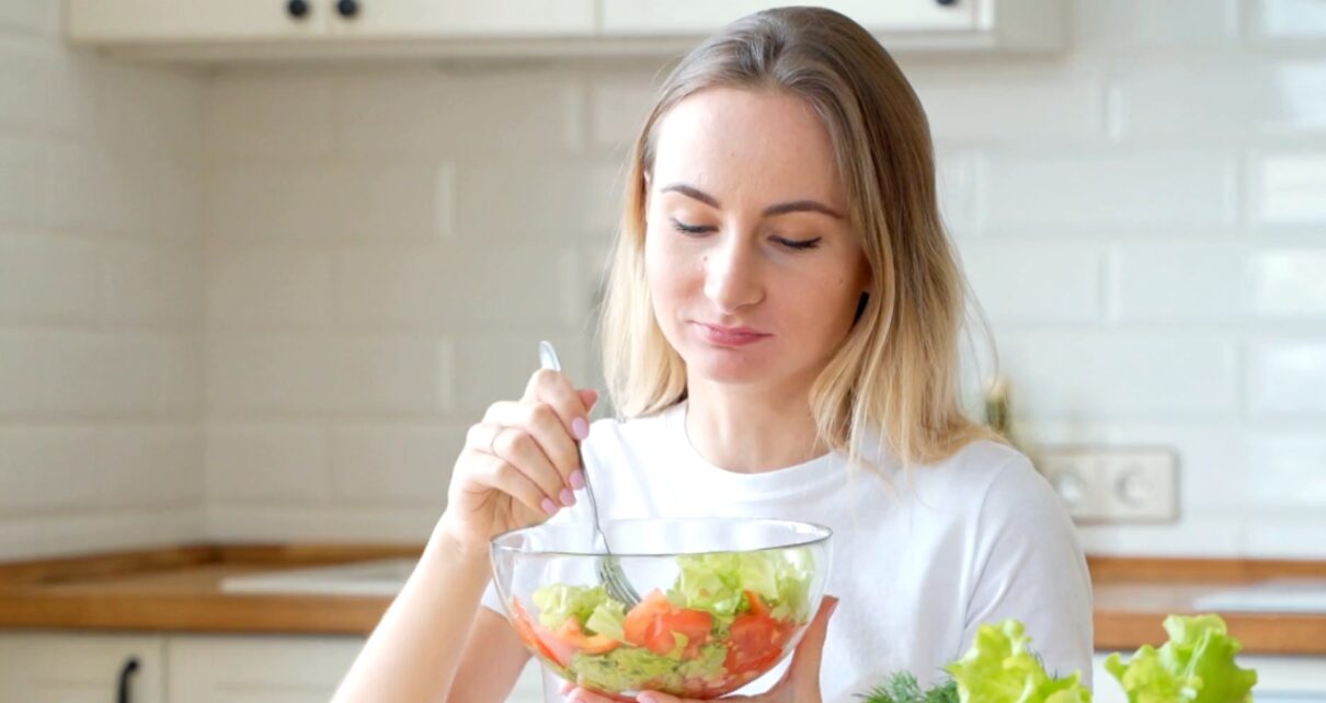 Woman with a bowl of fresh salad in a bright kitchen.