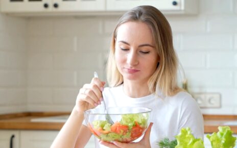 Woman with a bowl of fresh salad in a bright kitchen.