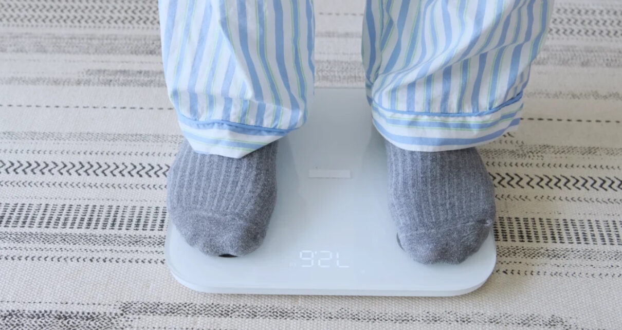 A person in striped pajamas and gray socks stands on a digital bathroom scale.
