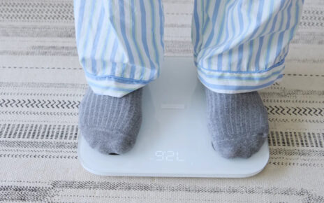 A person in striped pajamas and gray socks stands on a digital bathroom scale.