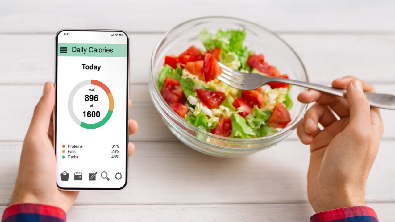 A person checks daily calorie intake on a phone beside a bowl of salad.