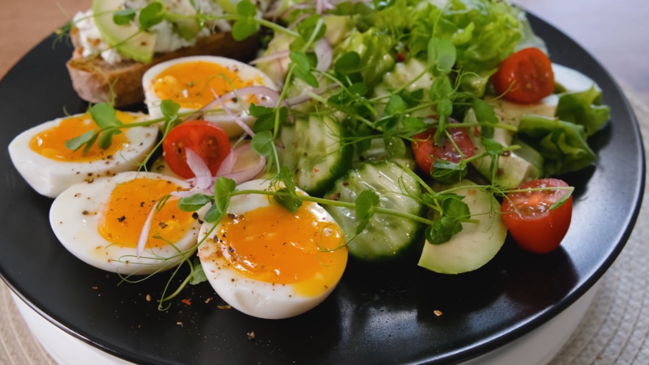 Keto meal with eggs, avocado, cucumber, tomatoes, and leafy greens.