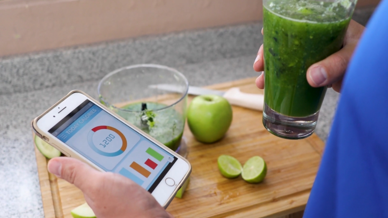 Person checks calorie intake on a phone while holding a green smoothie.