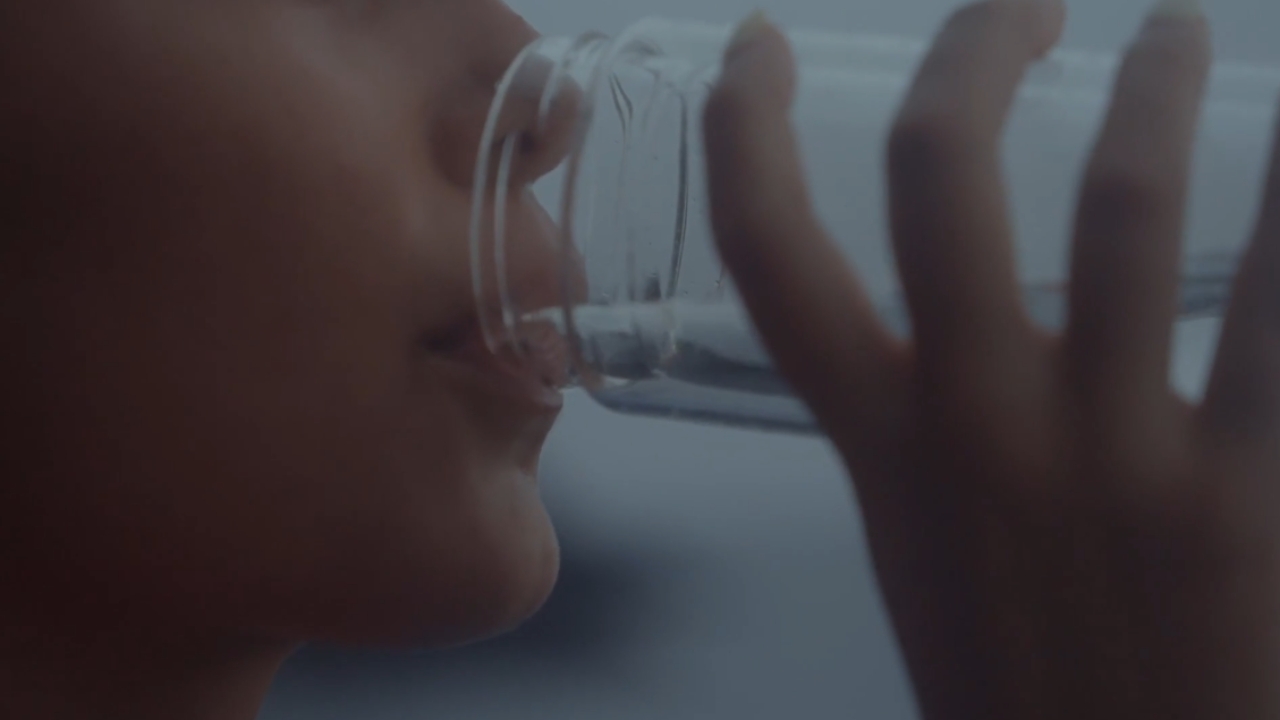 A person sips water through the rim of a clear glass.