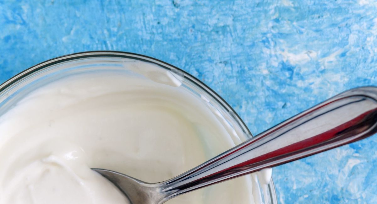 Bowl of thick white yogurt with a metal spoon on a blue background.